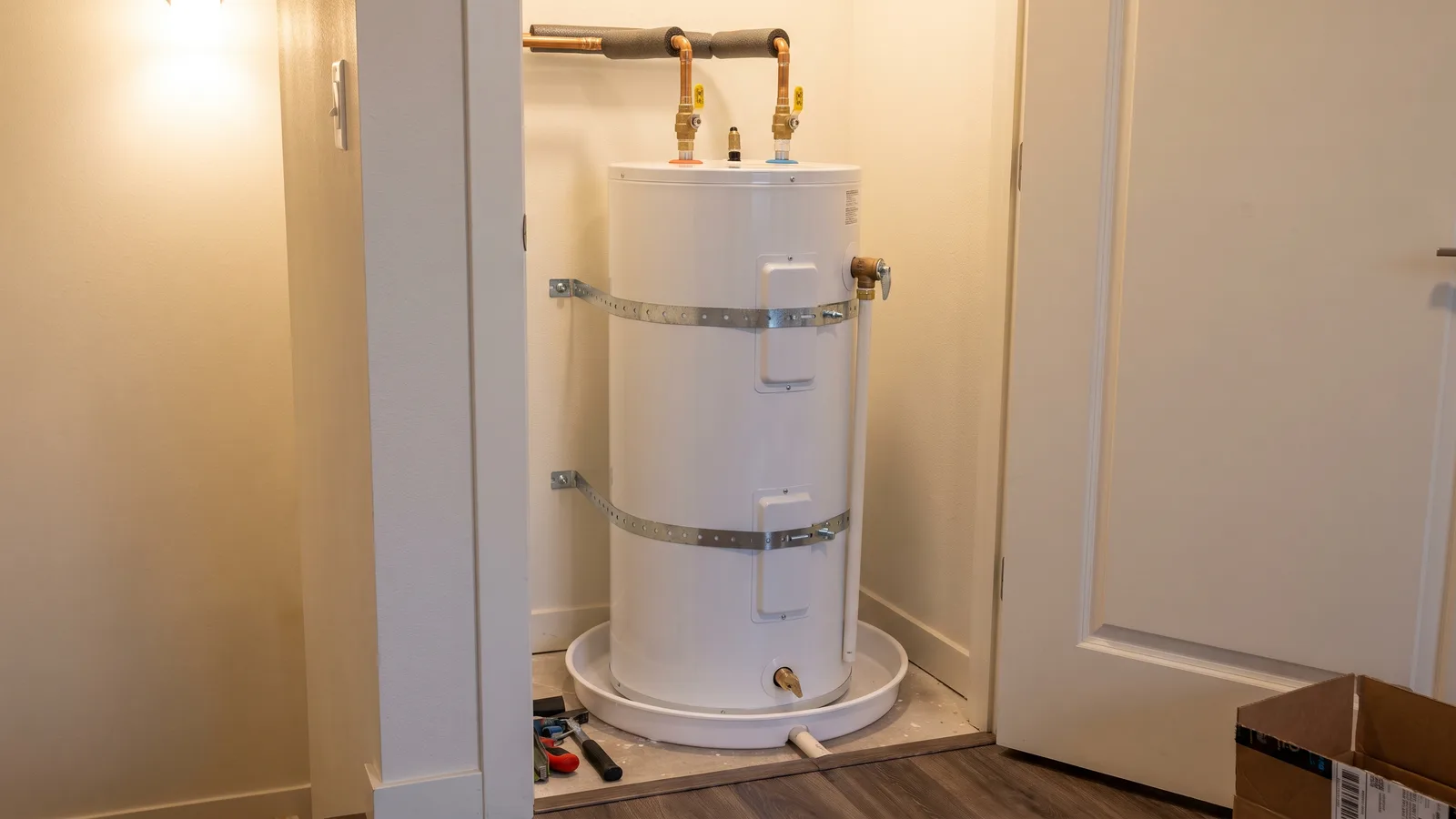 Electric hot water tank in a compact utility closet, strapped to the wall and standing in a drain pan